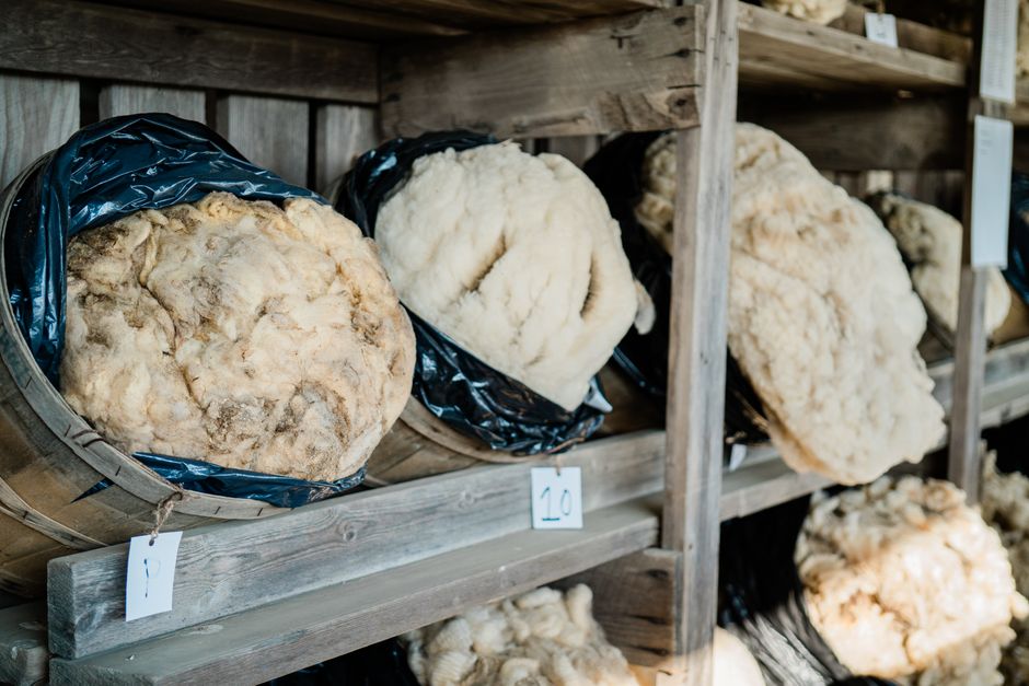 A display of raw wool bundles in sacks on rustic wooden shelves, organized in a market setting.