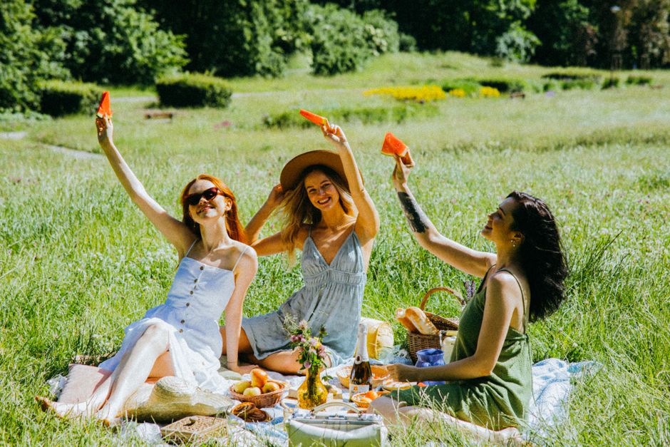 Three cheerful women having a summer picnic with watermelon slices in a sunny meadow.