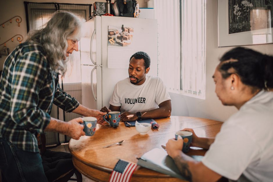 Three volunteers sharing coffee and ideas in a cozy kitchen setting, promoting community e