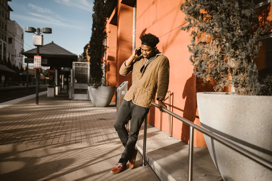 Casual young man leaning on handrail and using smartphone on a sunny day.