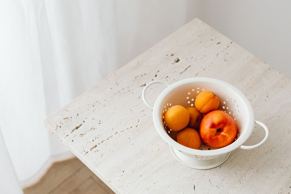 Top view of apricots and a peach in a white colander on a rustic table, perfect for summer