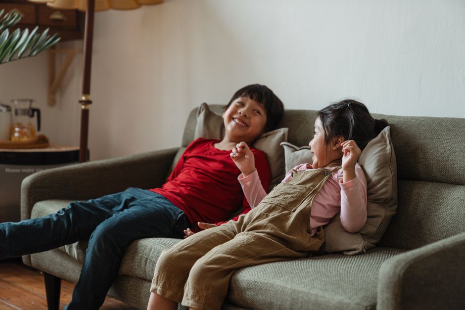 Two kids smiling and enjoying leisure time on a sofa in a warm living room setting.