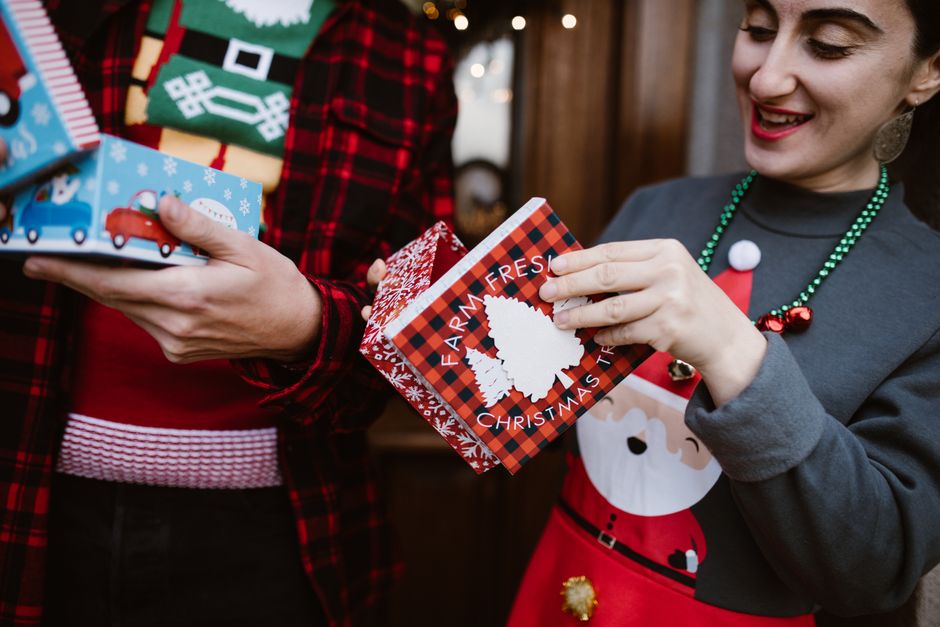Two people joyfully exchanging Christmas gifts, each bearing holiday-themed designs, indoo