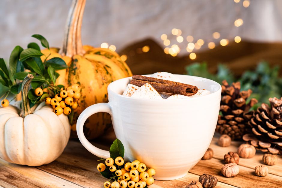 Warm autumn setup with coffee, pumpkins, cinnamon, and rustic decor on a wooden table.