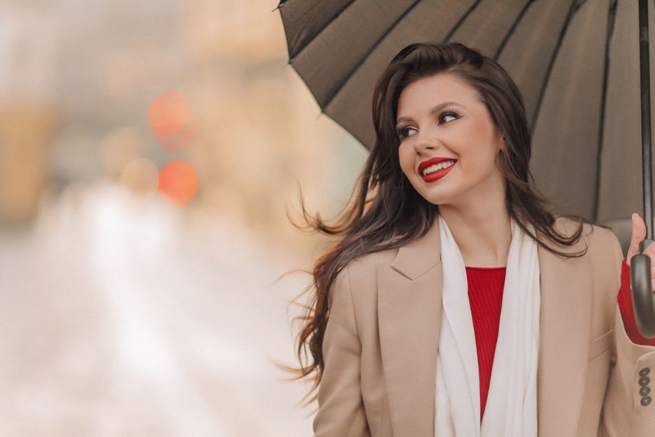 Chic woman in coat with umbrella, smiling on a city street. Elegant fashion photography.