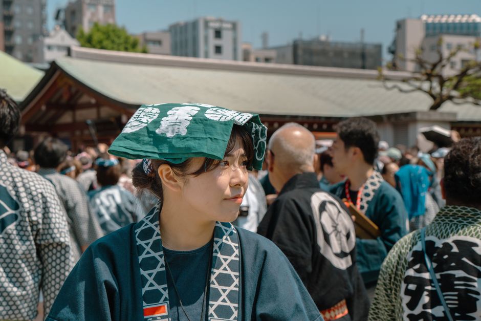 A woman in traditional attire at a vibrant Tokyo festival, surrounded by a lively crowd.