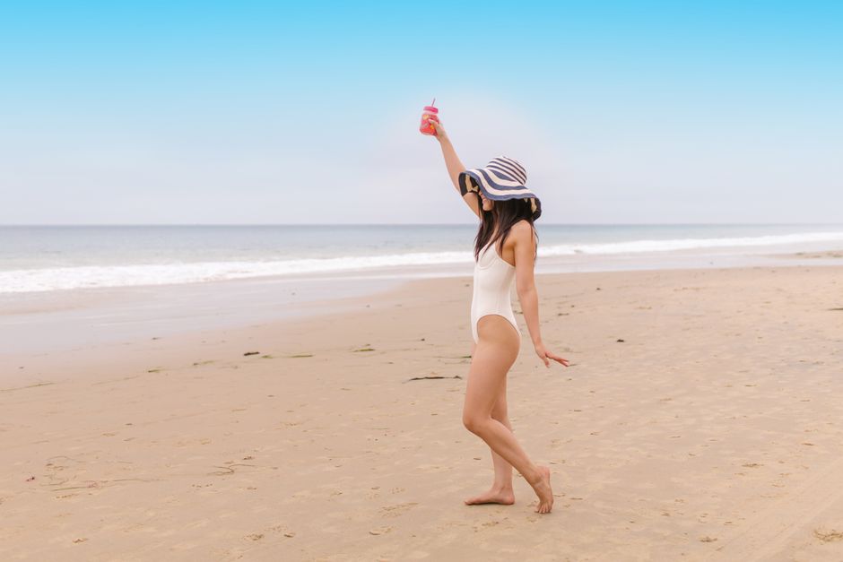 Young woman in swimsuit with drink on the beach enjoying a sunny day.
